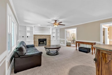 Carpeted living room featuring a ceiling fan, ornamental molding, a brick fireplace, and built in shelves