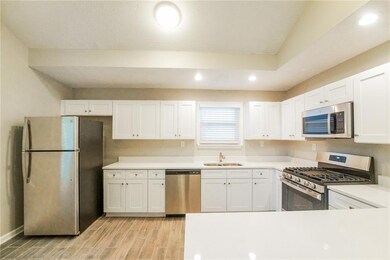 Kitchen featuring appliances with stainless steel finishes, a sink, white cabinetry, wood finish floors, and recessed lighting