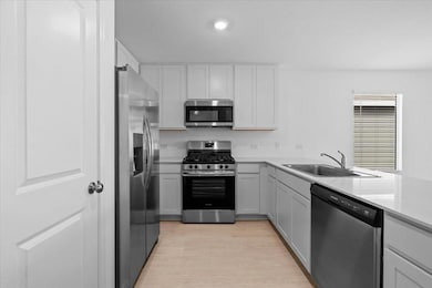 Kitchen with appliances with stainless steel finishes, light wood-style floors, a peninsula, white cabinets, and recessed lighting