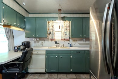 Kitchen with freestanding refrigerator, green cabinets, light countertops, a textured ceiling, and dishwasher