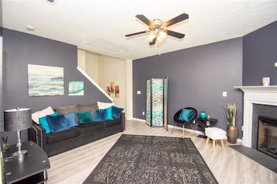 Living area featuring a glass covered fireplace, ceiling fan, wood finished floors, and a textured ceiling