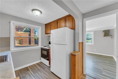 Kitchen with white appliances, brown cabinetry, light countertops, light wood finished floors, and a textured ceiling