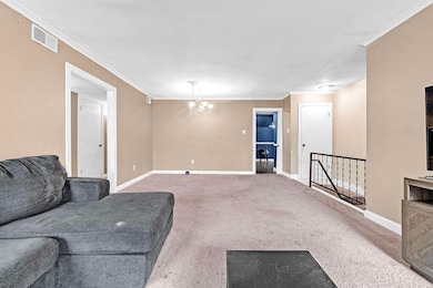 Carpeted living room featuring crown molding and a chandelier