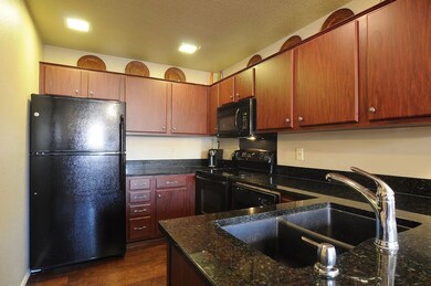 Kitchen with black appliances, dark wood-style floors, dark stone countertops, and a textured ceiling
