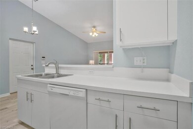 Kitchen with vaulted ceiling, light wood-type flooring, ceiling fan with notable chandelier, white dishwasher, and sink