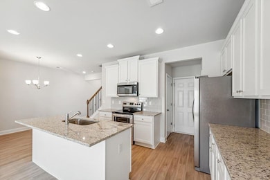 Kitchen with sink, light stone counters, a center island with sink, white cabinets, and appliances with stainless steel finishes