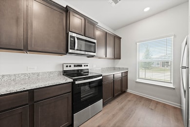 Kitchen with appliances with stainless steel finishes, dark brown cabinets, light wood-style flooring, light stone countertops, and recessed lighting