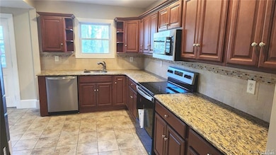 Kitchen with appliances with stainless steel finishes, decorative backsplash, light stone countertops, light tile patterned floors, and open shelves