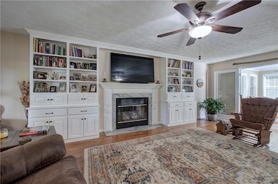 Living area with wood finished floors, a textured ceiling, a premium fireplace, and ceiling fan