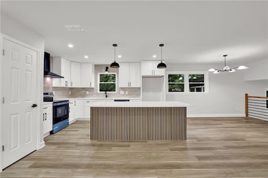 Kitchen with stainless steel range with electric cooktop, wall chimney exhaust hood, a center island, light countertops, and white cabinetry
