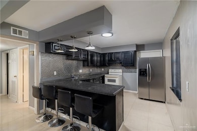 Kitchen featuring stainless steel refrigerator with ice dispenser, white electric range oven, a peninsula, backsplash, and light tile patterned floors