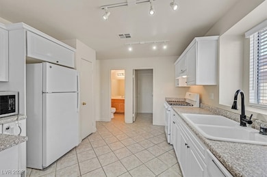 Kitchen featuring white appliances, white cabinets, light tile patterned floors, and rail lighting
