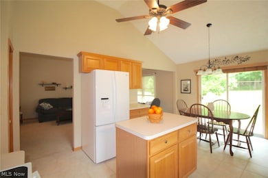 Kitchen with light tile patterned flooring, white fridge with ice dispenser, a center island, ceiling fan, and high vaulted ceiling