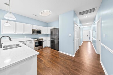 Kitchen with sink, hanging light fixtures, dark hardwood / wood-style flooring, white cabinets, and appliances with stainless steel finishes