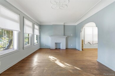 living room featuring arched walkways, hardwood / wood-style flooring, a brick fireplace, and ornamental molding