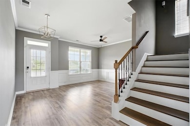 Foyer entrance with wood finished floors, stairs, crown molding, a chandelier, and a wainscoted wall