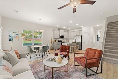 Living room with stairs, light wood finished floors, ceiling fan, a chandelier, and recessed lighting