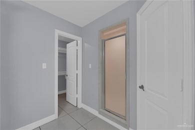 Full bath with tile patterned flooring, baseboards, a walk in closet, and a stall shower