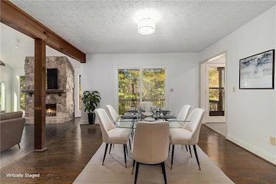 Dining space featuring dark wood-style flooring, beamed ceiling, a fireplace, and a textured ceiling