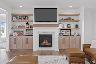 Living area with a glass covered fireplace, visible vents, light wood finished floors, and baseboards
