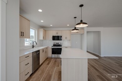 Kitchen featuring light brown cabinetry, appliances with stainless steel finishes, tasteful backsplash, a center island, and hanging light fixtures