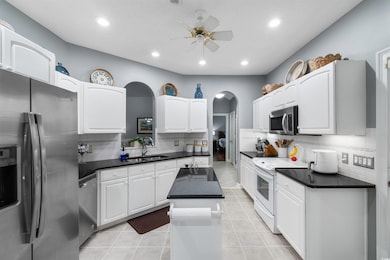 Kitchen featuring stainless steel appliances, arched walkways, ceiling fan, backsplash, and recessed lighting