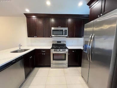 Kitchen featuring stainless steel appliances, decorative backsplash, light stone counters, dark brown cabinets, and light tile patterned floors