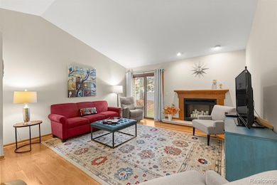 Living area featuring light wood-style flooring, a fireplace with raised hearth, and vaulted ceiling