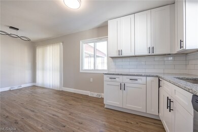 Kitchen featuring tasteful backsplash, white cabinets, light stone counters, hanging light fixtures, and light hardwood / wood-style flooring