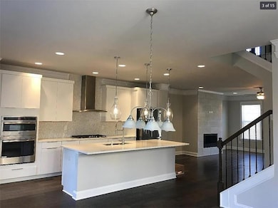Kitchen with light countertops, wall chimney range hood, dark wood-style floors, tasteful backsplash, and pendant lighting