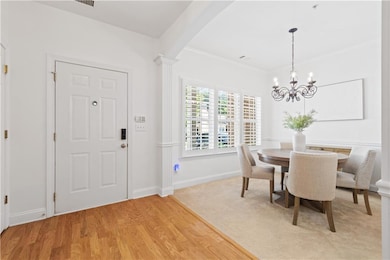Dining room with light wood-type flooring, a chandelier, crown molding, and decorative columns