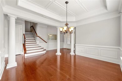 Unfurnished dining area featuring decorative columns, wood finished floors, stairway, a wainscoted wall, and a chandelier