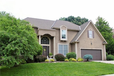 View of front facade featuring driveway, stucco siding, a front lawn, a garage, and roof with shingles