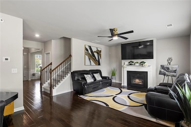 Living room with hardwood floors, stairs, a fireplace with flush hearth, ceiling fan, and baseboards