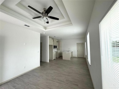 Unfurnished living room with a ceiling fan, visible vents, light wood finished floors, baseboards, and a raised ceiling