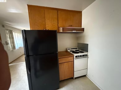 Kitchen with freestanding refrigerator, white range with electric stovetop, range hood, finished concrete flooring, and brown cabinetry