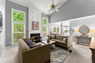 Living area with a fireplace, light colored carpet, a ceiling fan, and high vaulted ceiling