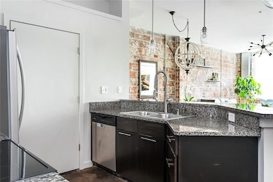 Kitchen featuring appliances with stainless steel finishes, brick wall, a chandelier, a sink, and a peninsula