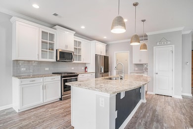 Kitchen with appliances with stainless steel finishes, ornamental molding, light wood-style floors, tasteful backsplash, and white cabinetry