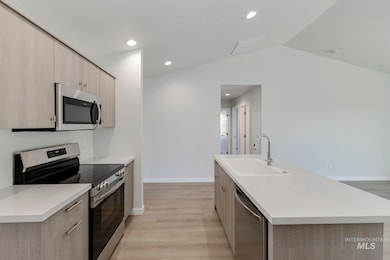 Kitchen with appliances with stainless steel finishes, light brown cabinetry, light countertops, recessed lighting, and lofted ceiling