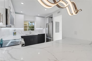 Kitchen featuring visible vents, stainless steel appliances, a sink, dark cabinetry, and light stone counters