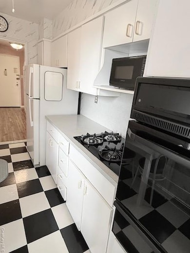 Kitchen with wall oven, light flooring, white cabinetry, light countertops, and fridge