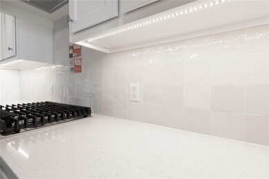 Kitchen view of stainless steel gas cooktop, light stone counters, white cabinetry, and tasteful backsplash