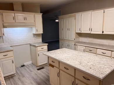 Kitchen featuring light countertops, decorative backsplash, ceiling fan, light wood-style floors, and under cabinet range hood