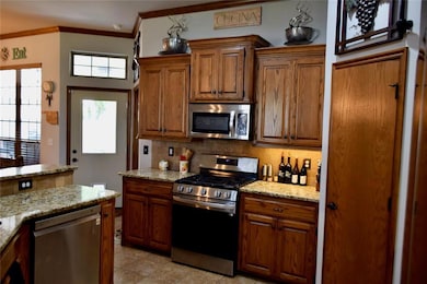 Kitchen with stainless steel appliances, tasteful backsplash, brown cabinetry, crown molding, and light stone countertops