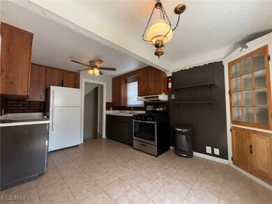 Kitchen with ceiling fan, white refrigerator, light tile patterned floors, sink, and stainless steel range