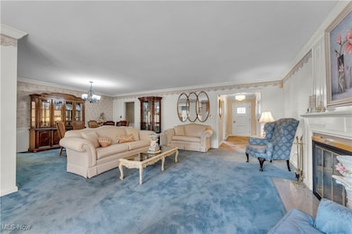 Carpeted living room with wallpapered walls, ornamental molding, a chandelier, and a premium fireplace
