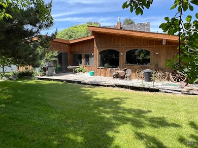Rear view of house with a deck, a chimney, a lawn, and board and batten siding