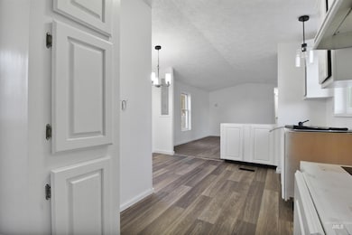 Kitchen with lofted ceiling, white cabinetry, white stove, pendant lighting, and a textured ceiling