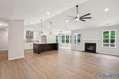 Unfurnished living room with light wood finished floors, lofted ceiling, a fireplace with flush hearth, and ceiling fan